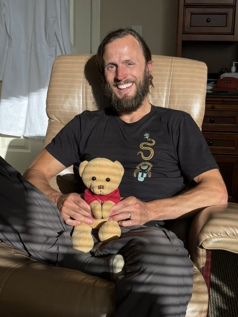 Duke smiling in a sunlit armchair, holding a small teddy bear
